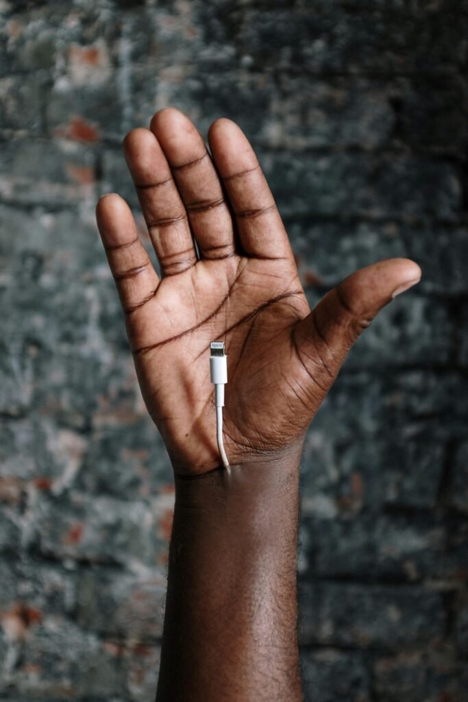 Close-up of a hand holding a charging cable against a textured brick wall background.